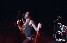 a man singing into a microphone on a stage with a drum set in the background and the words imgplay below him