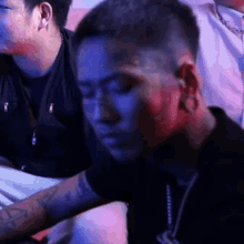 a man with a tattoo on his arm is sitting in a dark room with other men .