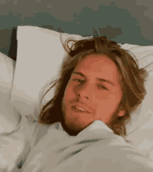 a man with long hair is laying in a bed