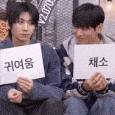 two young men are sitting next to each other holding signs in their hands in korean .