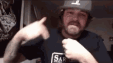 a man with a beard wearing a hard hat and a blue shirt is pointing at the camera .