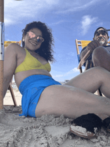 a woman in a bikini sits on a beach next to a man