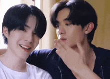 two young men are sitting next to each other and one is touching the face of the other .