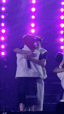 two men hugging on a stage with the word joiuoii on the bottom right