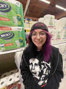 a girl with purple hair is standing in front of a stack of nicky elite toilet paper