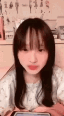 a girl with long hair and bangs is sitting in front of a tablet .