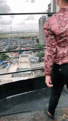 a man in a snakeskin shirt stands on a balcony overlooking a city