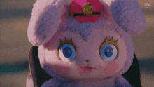a stuffed animal with blue eyes and a pink hat is being held by a person .