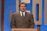 a man in a suit and tie is standing at a podium with his hands behind his back .
