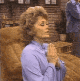 a woman in a blue shirt is praying while sitting on a couch