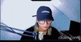 a person wearing a hat and glasses is sitting in front of a microphone .