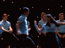a group of people in blue shirts are dancing
