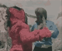 a man in a blue shirt is fighting another man in a red jacket in a blurry photo .