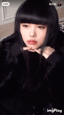 a woman with long black hair and bangs is wearing a black fur coat and looking at the camera .