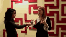 a woman is holding a microphone and talking to another woman in front of a maze wall