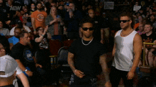 a man wearing sunglasses stands in front of a crowd wearing a shirt that says " aew "