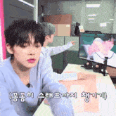 a boy in a blue sweater sits at a desk in front of a computer monitor with chinese writing on it