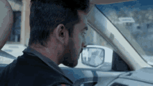a man is driving a car and looking at the side mirror