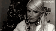 a woman is standing in front of a christmas tree wearing a fur coat and earrings .