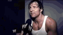 a man in a white tank top is talking into a microphone in a dark room .