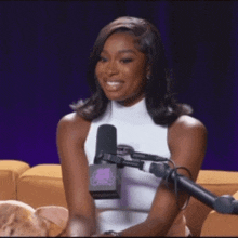 a woman in a white tank top is sitting in front of a microphone on a couch .