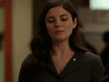 a woman wearing a black jacket with a gold button on the collar is looking down .