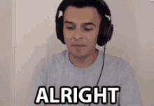 a man wearing headphones is sitting in front of a computer screen and says `` alright '' .