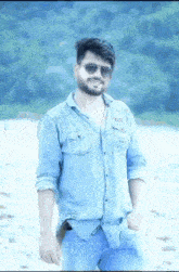 a man wearing sunglasses and a denim shirt is standing on a beach .