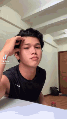 a young man is sitting at a table with his hand on his forehead and a tiktok sticker on the bottom right