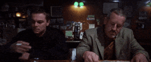 two men are sitting at a bar smoking cigarettes and drinking beer