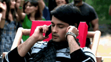a man sitting in a chair talking on a cell phone with a watch on his wrist
