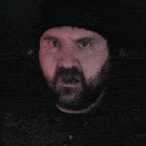 a man with a beard is wearing a black hat and headphones and his eyes are closed .