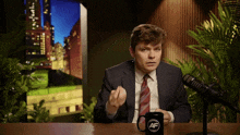 a man in a suit and tie sitting in front of a microphone with a mug that says af