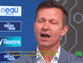 a man speaking in front of a sign that says neau water