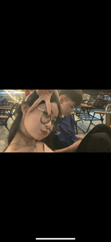a boy and a girl are sitting next to each other and the girl is making a peace sign with her hands .