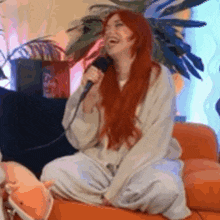 a woman with long red hair is sitting on a couch holding a microphone .