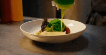 a close up of a plate of food with broccoli and sauce being poured on it