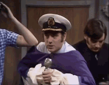 a man in a captain 's hat is holding a sword while being held by two other men .
