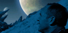 a man in a blue shirt looks at a planet in the sky