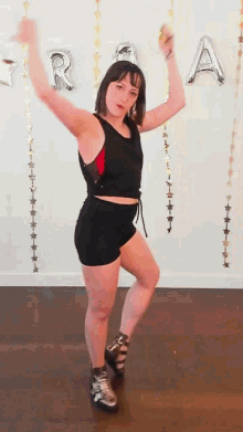 a woman in a black tank top and shorts is dancing in front of balloons with the letter a on them