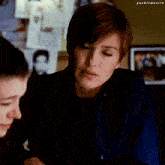 a woman in a blue shirt is talking to another woman in a dark room