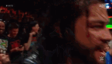 a man with long hair is screaming in front of a green screen with the word live on it