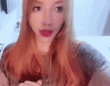 a woman with long red hair is taking a selfie with her phone .