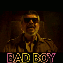 a man wearing sunglasses stands in front of a sign that reads bad boy