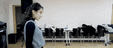 a woman stands in a room with chairs and a table