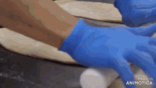 a person wearing blue gloves is rolling a piece of dough on a table .