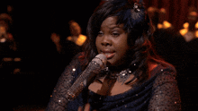 a woman singing into a silver microphone with a feather in her hair