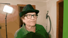 an elderly woman wearing a hat and glasses stands in front of a green screen
