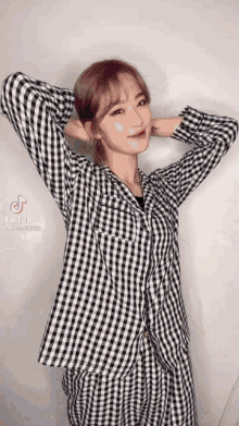 a woman in a plaid shirt is standing with her hands behind her head and smiling .