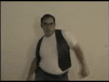 a man in a white shirt and a black vest is standing in front of a wall .